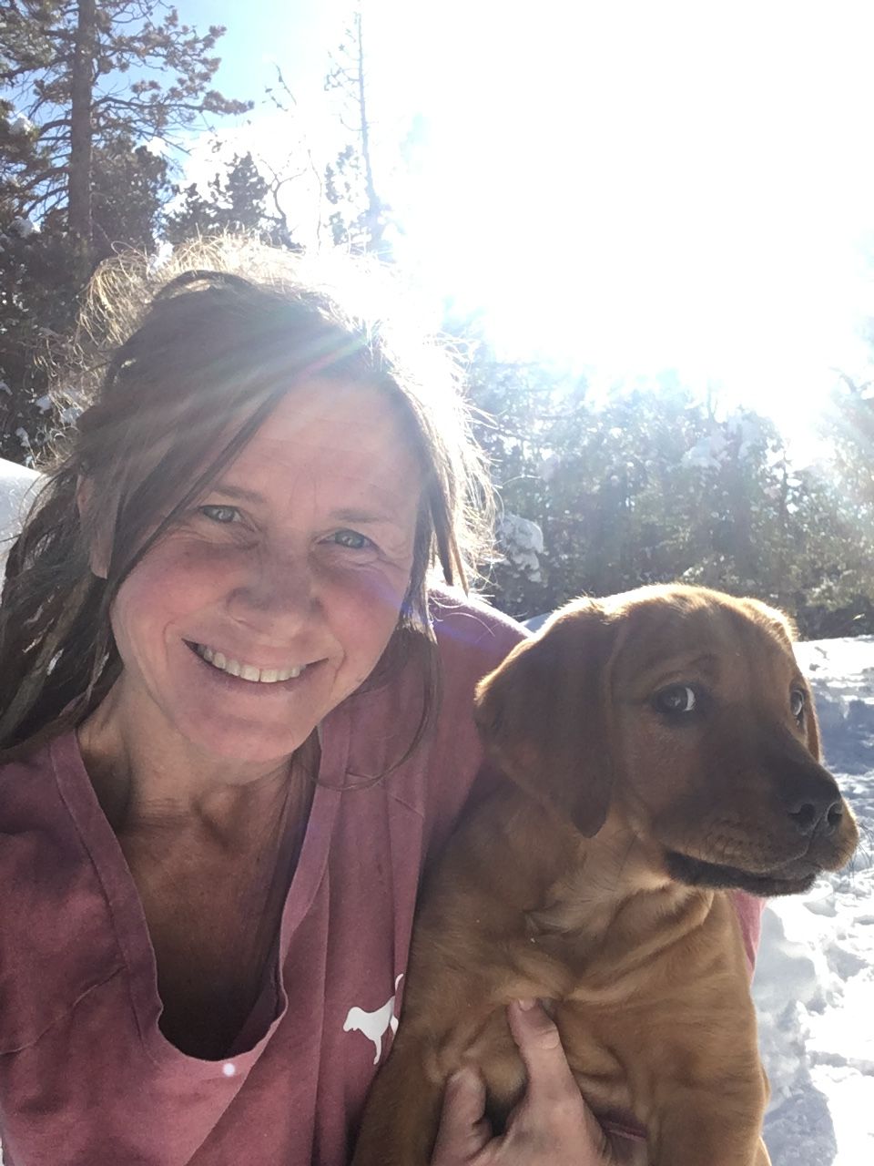 Jaime smiling in the winter sun, holding a red lab puppy
